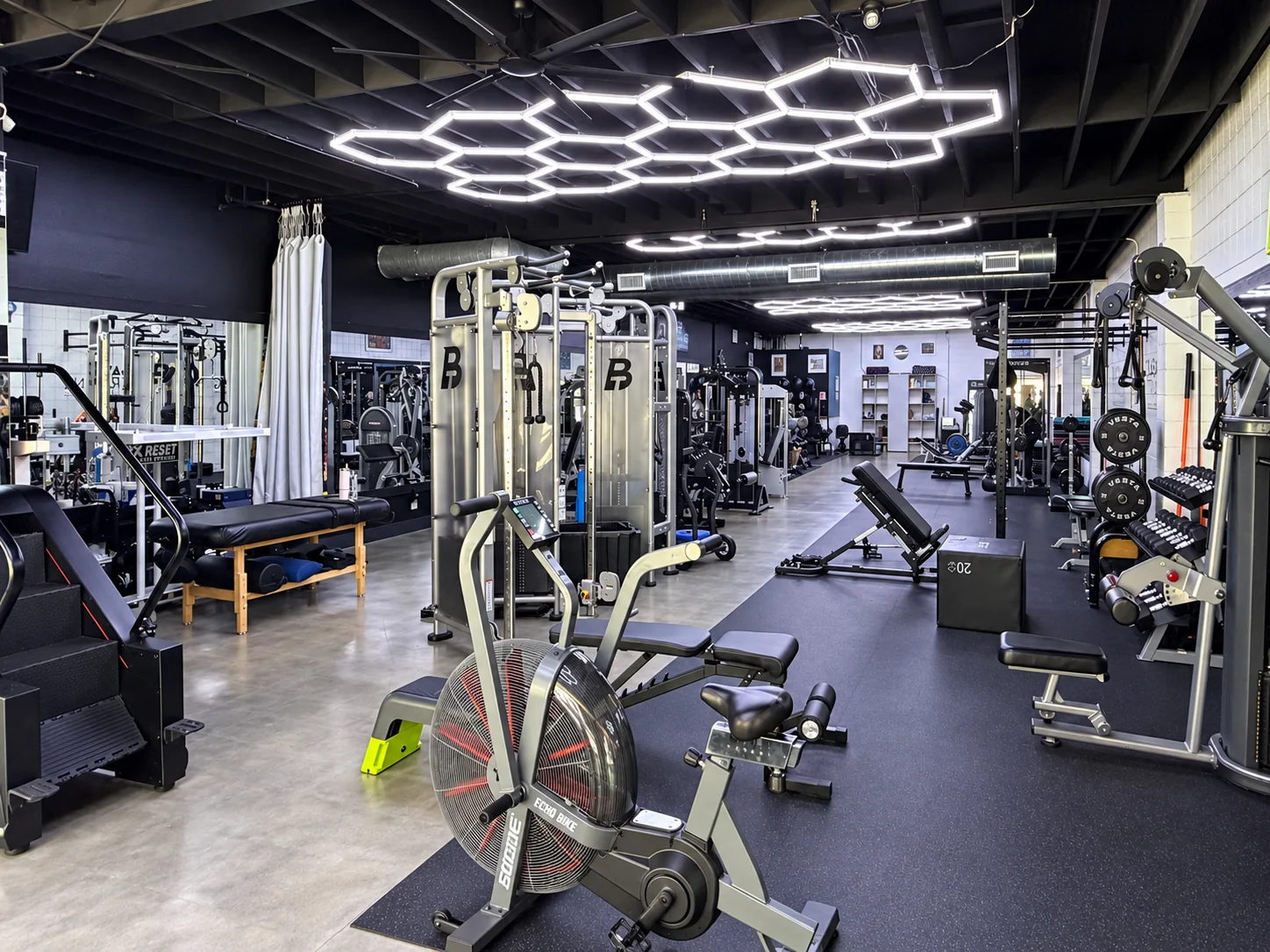 Wide view of BASIC Training's cable machines, benches and training floor beneath hexagonal ceiling lights