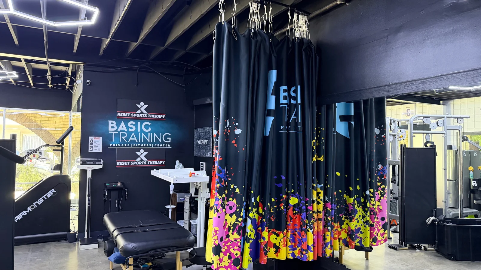 Recovery area with massage table, branded signage and a colorful privacy curtain