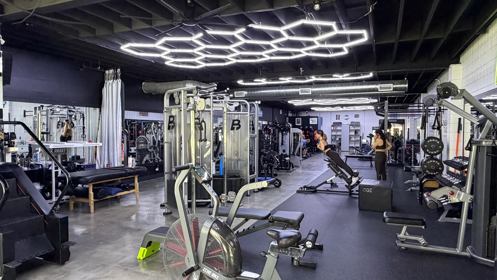 Wide view of BASIC Training's cable machines, benches and training floor beneath hexagonal ceiling lights