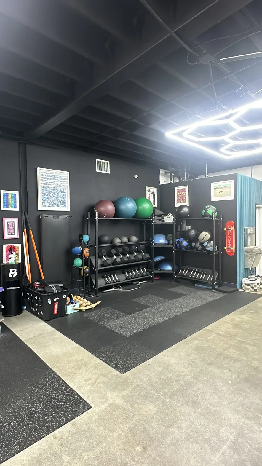 Accessories corner with medicine balls, dumbbells and curated framed art on a black wall at BASIC Training